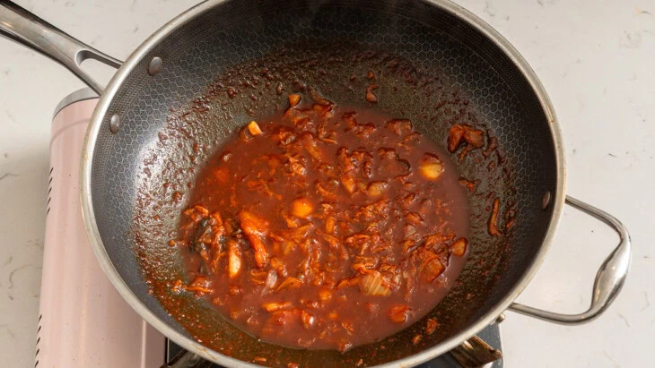 Cooking down kimchi and sauce in a wok.