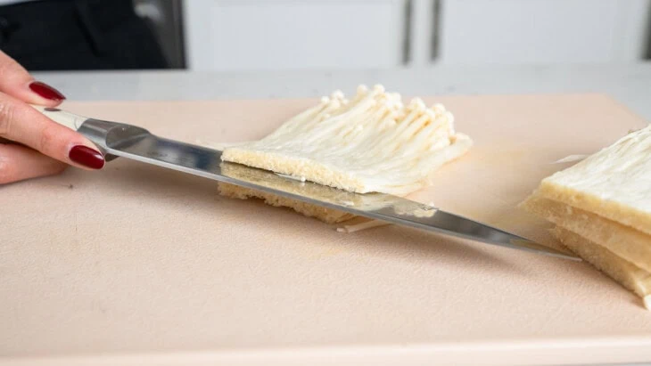 Slicing enoki mushrooms into layers.