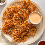 A top down view of a plate of fried enoki mushrooms with dipping sauces nearby.