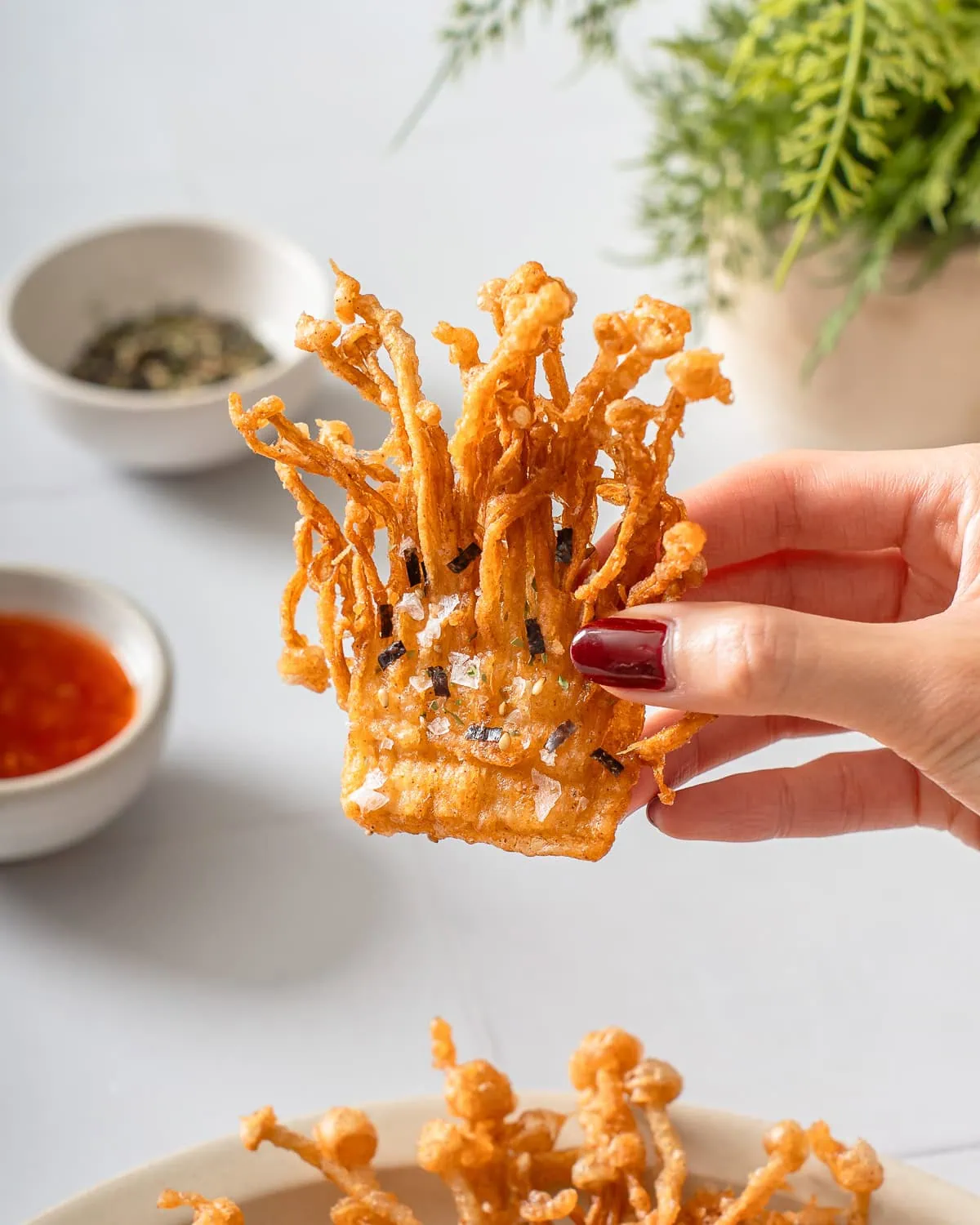 A hand holding up fried enoki mushrooms.