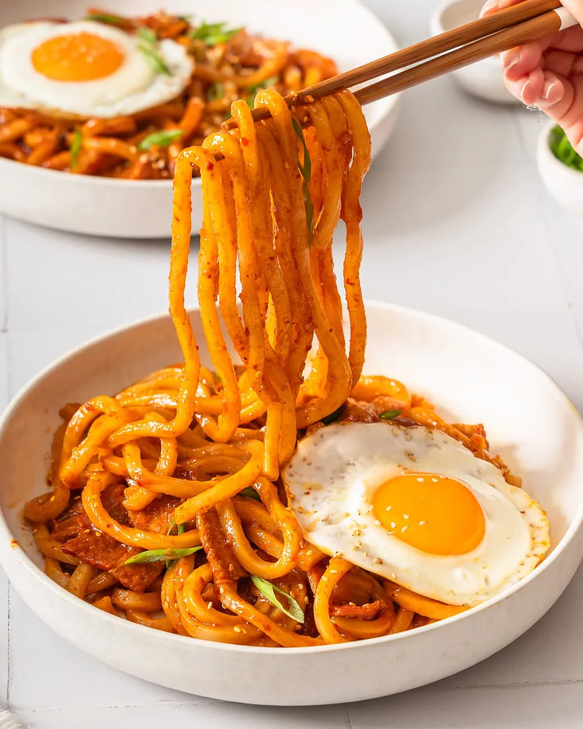 Noodles being lifted up from a plate with a pair of chopsticks.