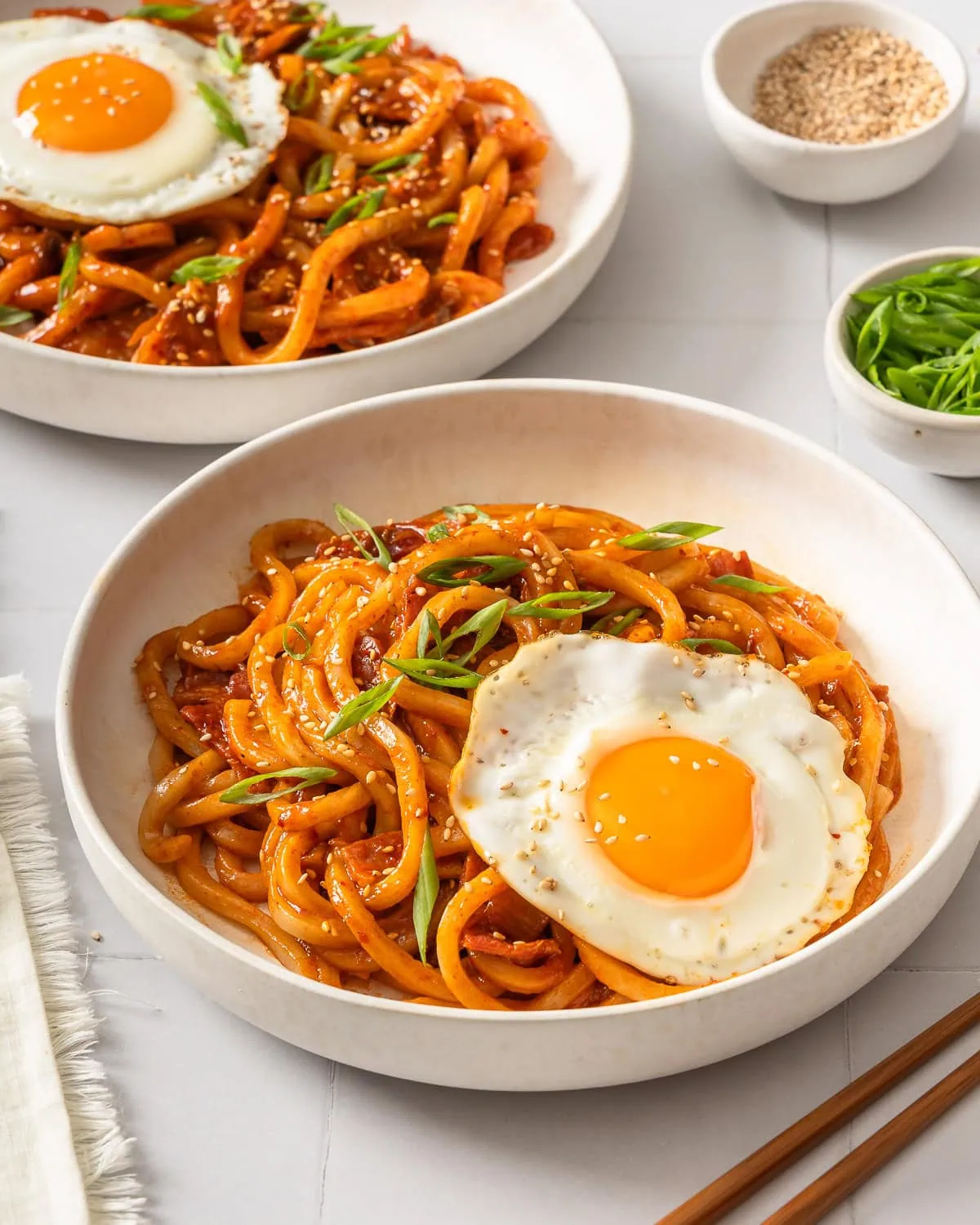 Two plates of kimchi udon topped fried eggs.