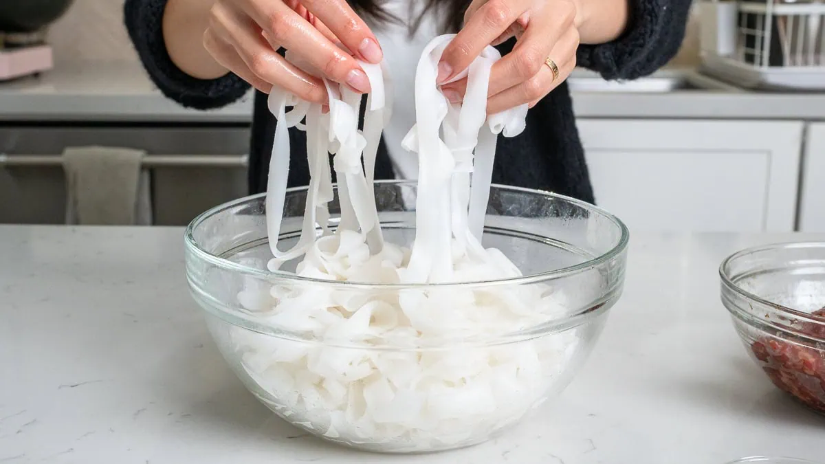 Loosening up fresh rice noodles in a glass bowl.