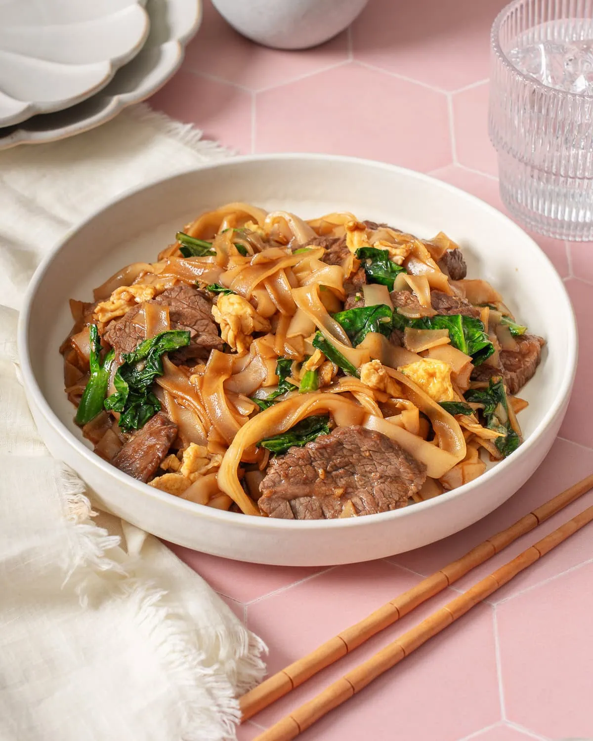 A plate of pad see ew surrounded by table settings.