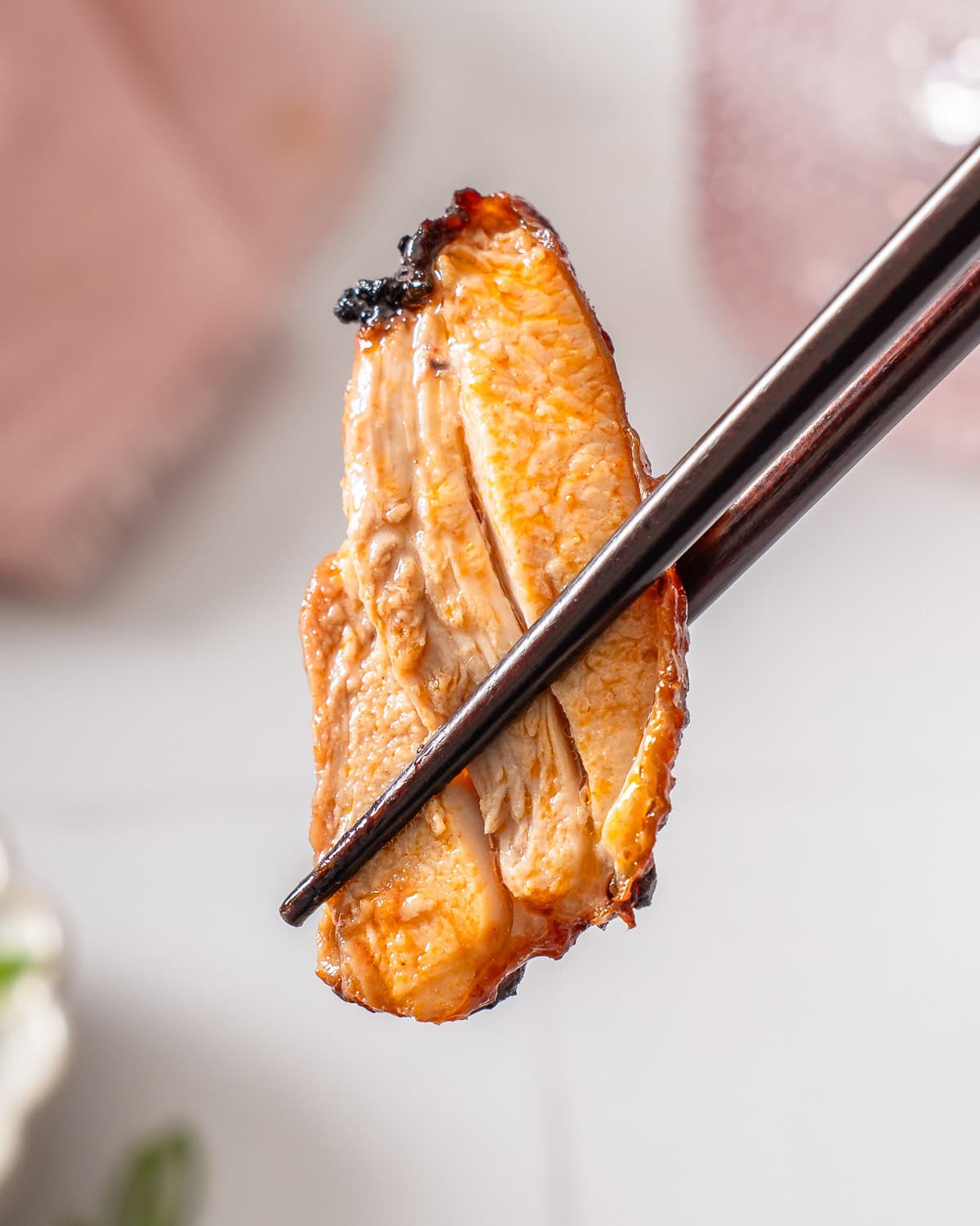 A slice of gochujang chicken held up by a pair of chopsticks.