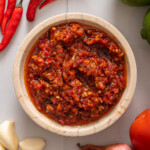 A top down view of a bowl of sambal oelek surrounded by ingredients.