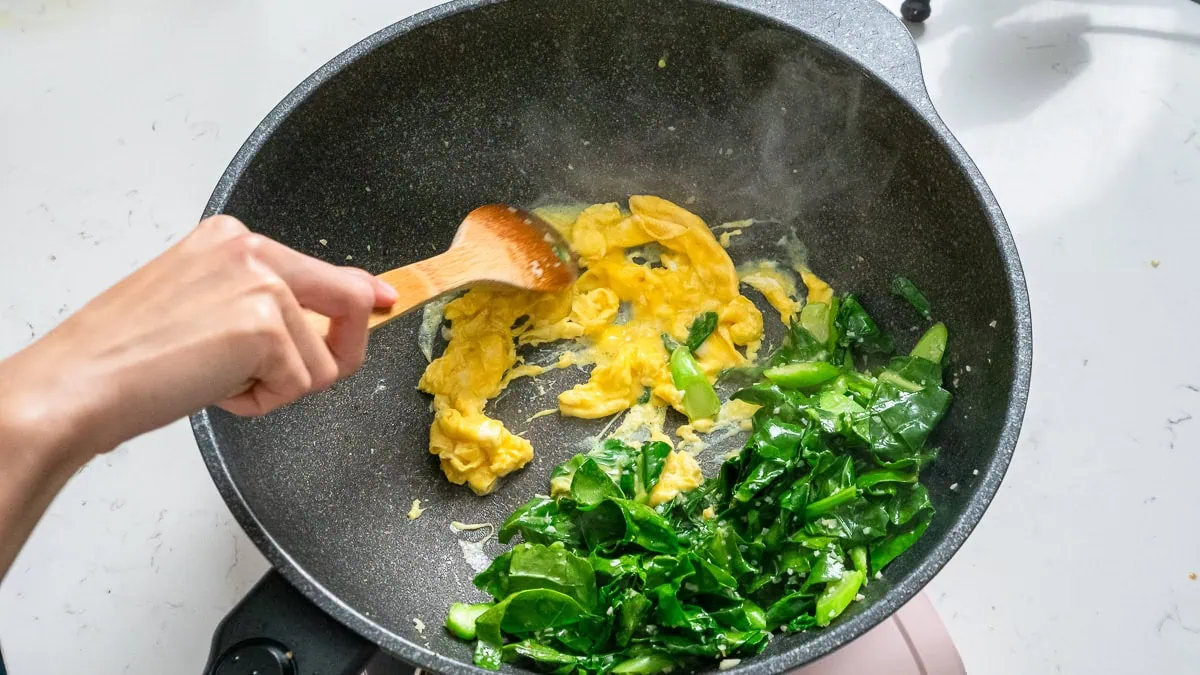 Scrambling eggs in the side of a wok.