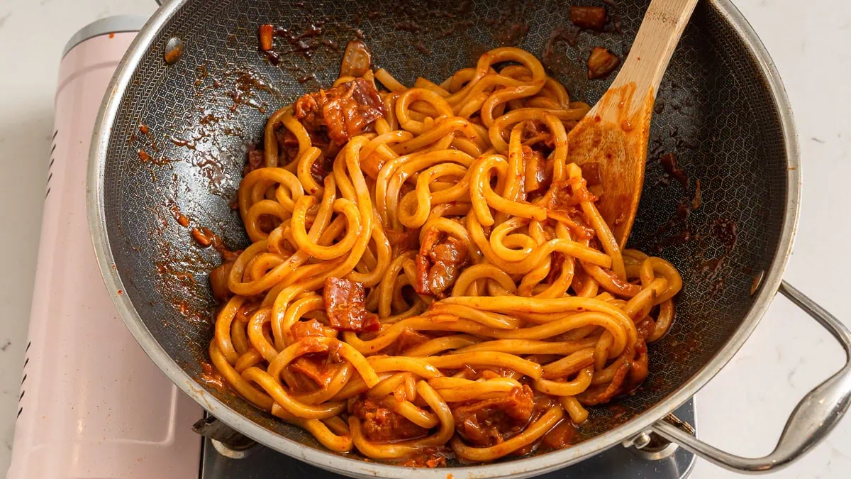 Tossing together kimchi udon in a wok.