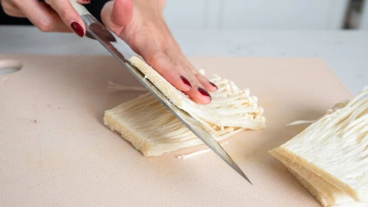 Slicing enoki mushrooms into layers.