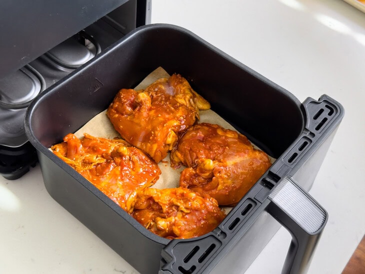 Marinated chicken thighs placed inside a lined air fryer basket.