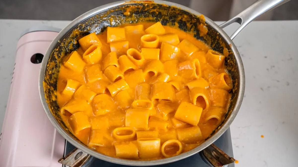 Mezza rigatoni tossed in sauce inside a large skillet.