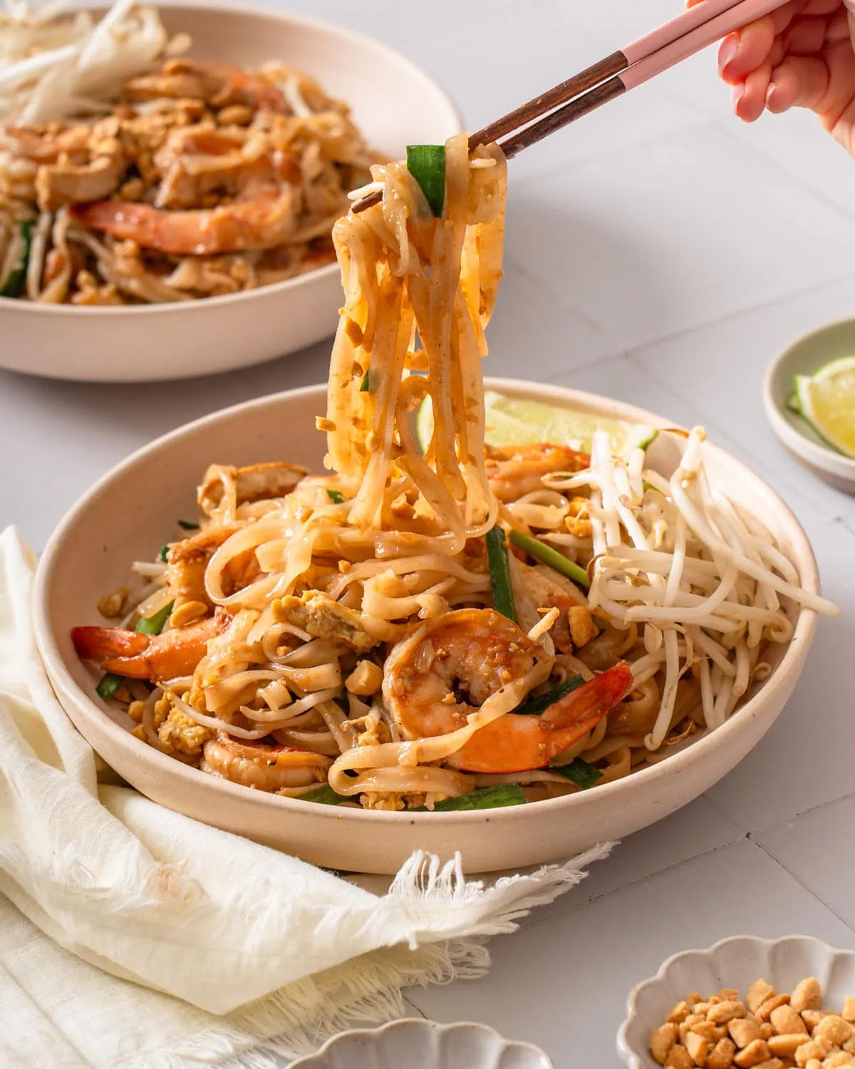 A pair of chopsticks lifting up pad thai from a plate.