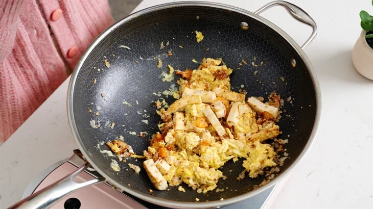 Eggs, tofu, shrimp, and aromatics tossed in a wok.