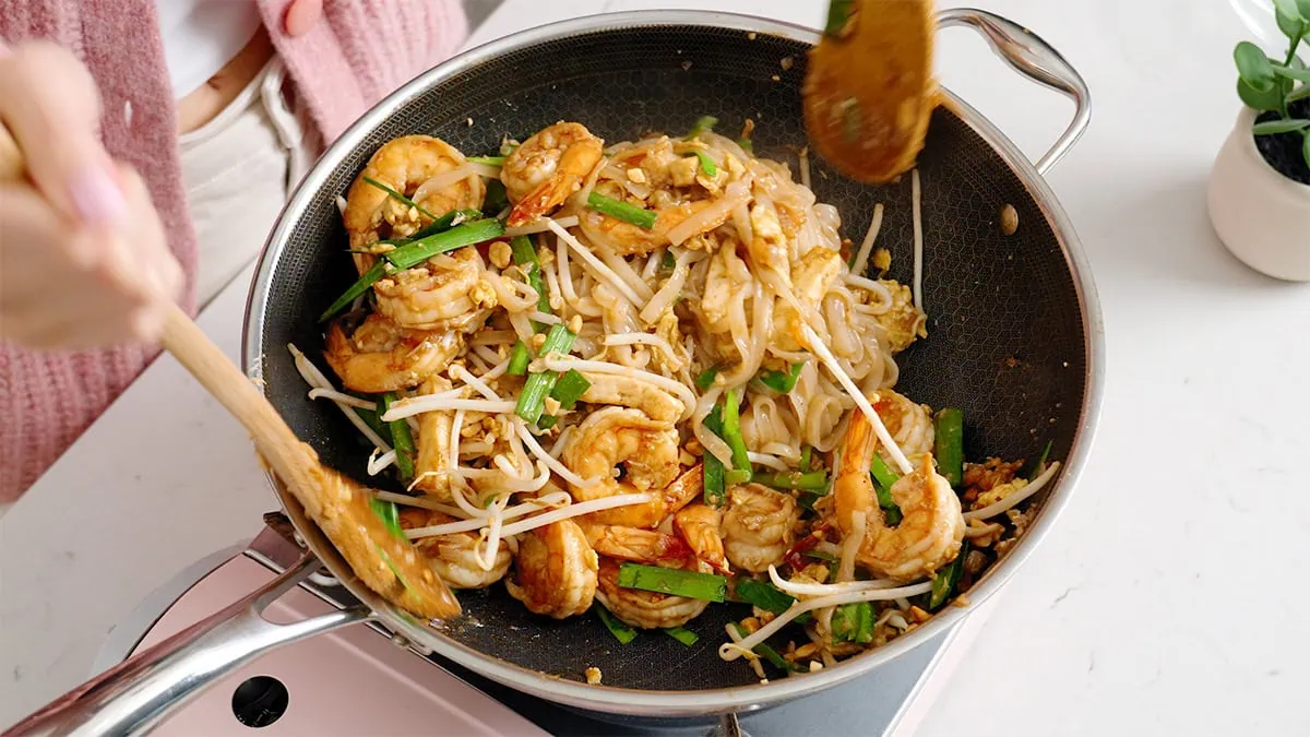 Shrimp pad thai tossed together inside a wok.