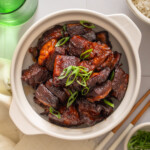 A topdown view of a bowl of chinese braised pork belly surrounded by table settings.