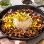 A skillet filled with beef pepper rice surrounded by table settings.