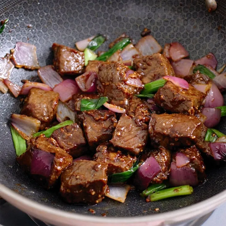 Beef and onions tossed inside a wok.
