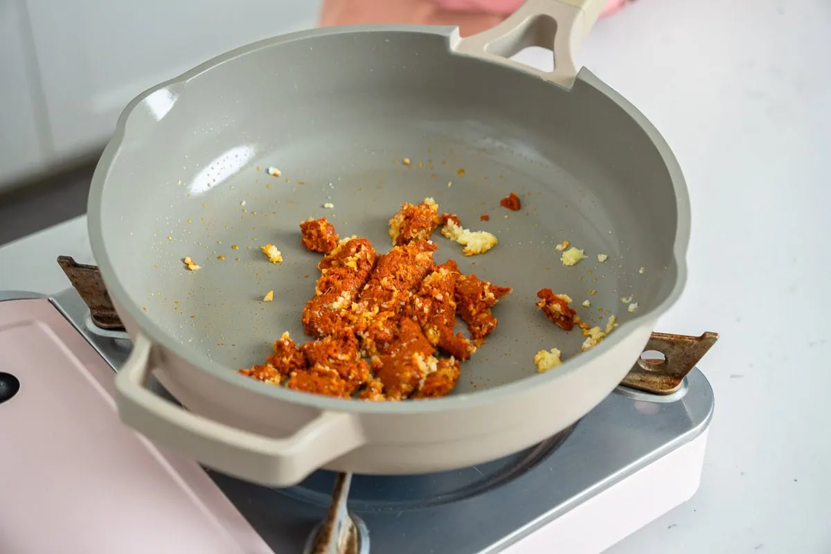 Sautéing minced aromatics and red curry paste in a deep skillet.