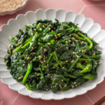A plate of sigeumchi namul surrounded by table settings.