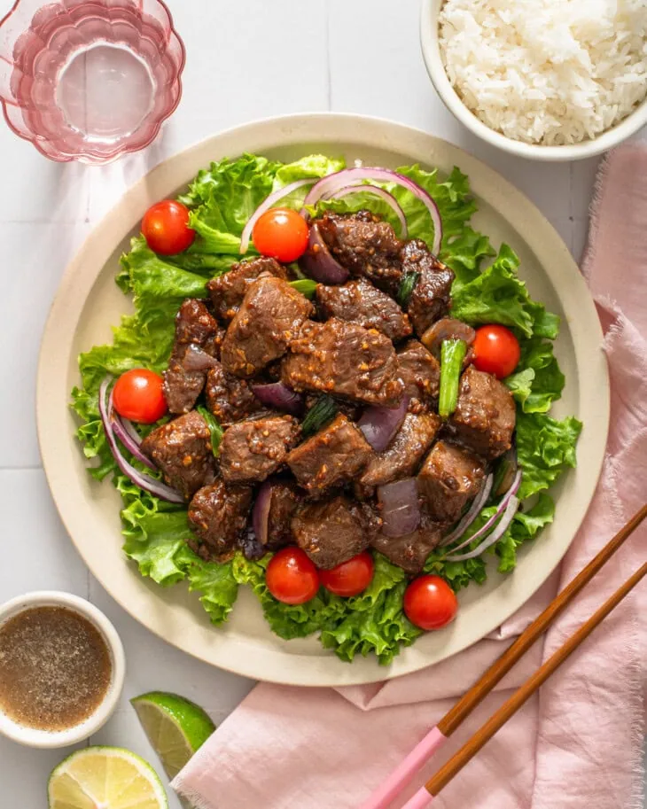 A plate of Vietnamese shaking beef surrounded by table settings.
