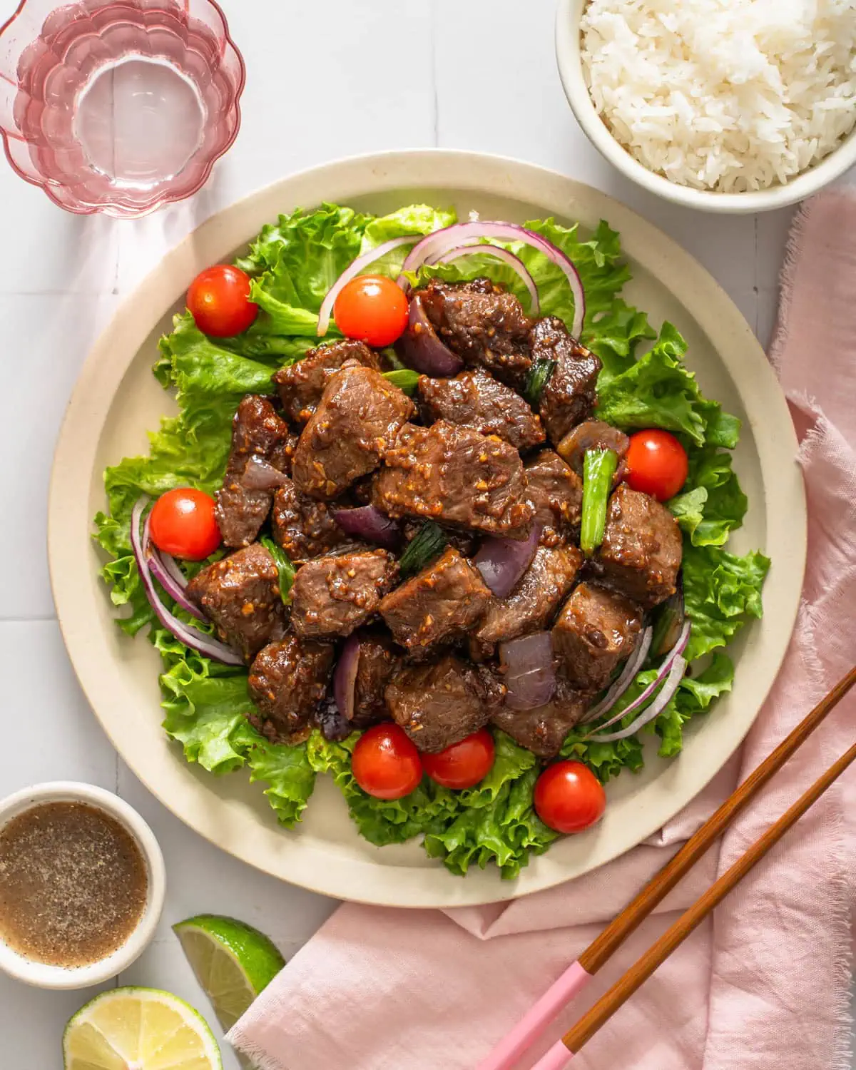 A plate of Vietnamese shaking beef surrounded by table settings.