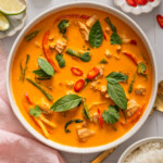 A bowl of Thai red curry surrounded by table settings.