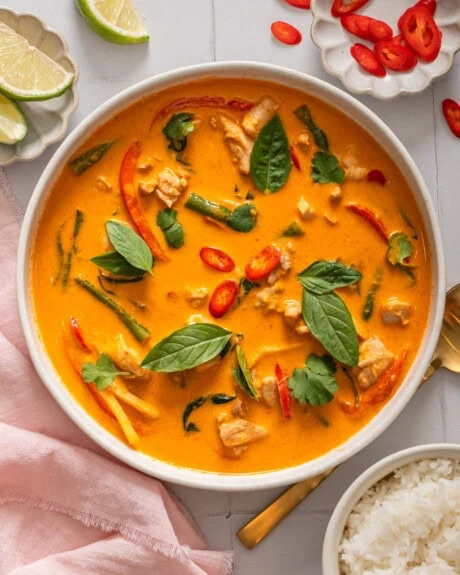 A bowl of Thai red curry surrounded by table settings.