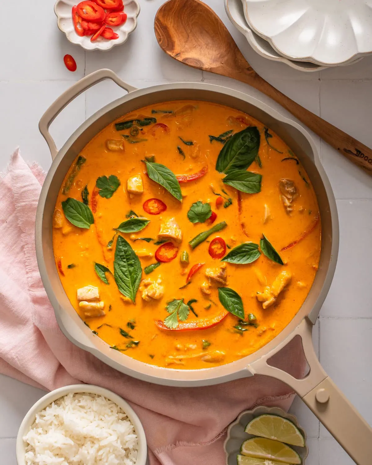 A top down view of a deep skillet filled with Thai red curry surrounded by table settings.