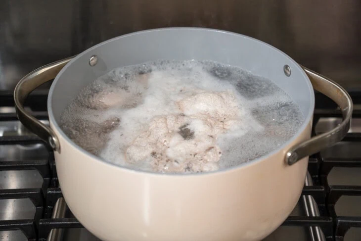 Pork belly being parboiled in a large pot.