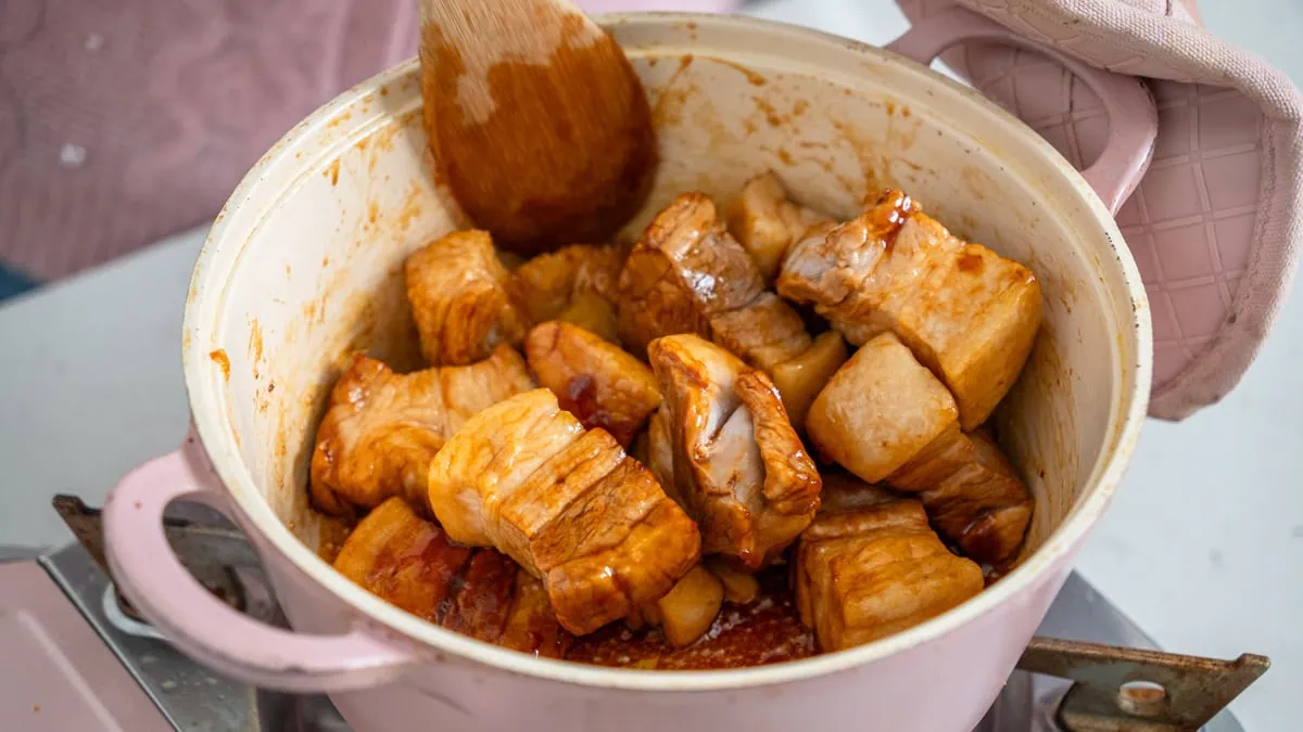 Mixing pork belly in a pot with caramel and spices.