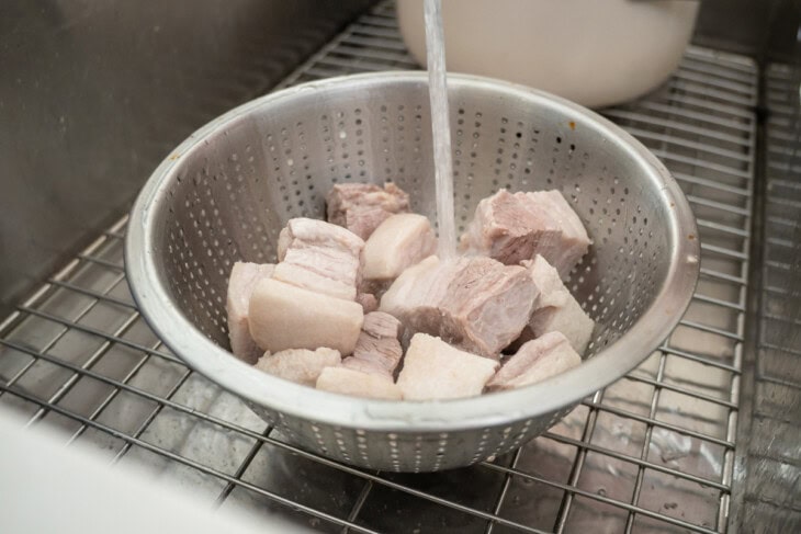 Rinsing parboiled pork belly in a sink.