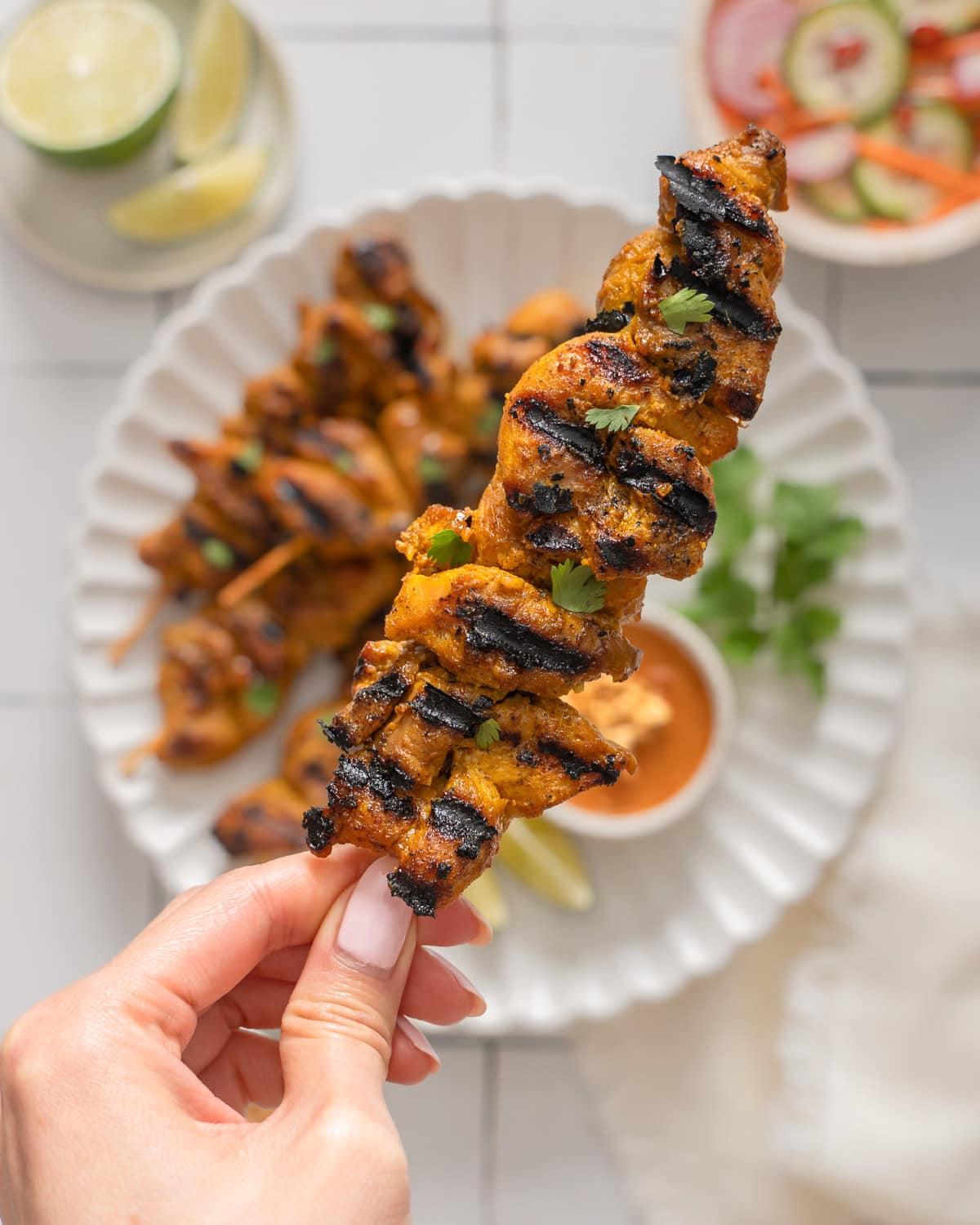 A hand holding up a skewer of Thai chicken satay.