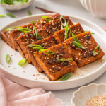A plate of Korean braised tofu surrounded by table settings.