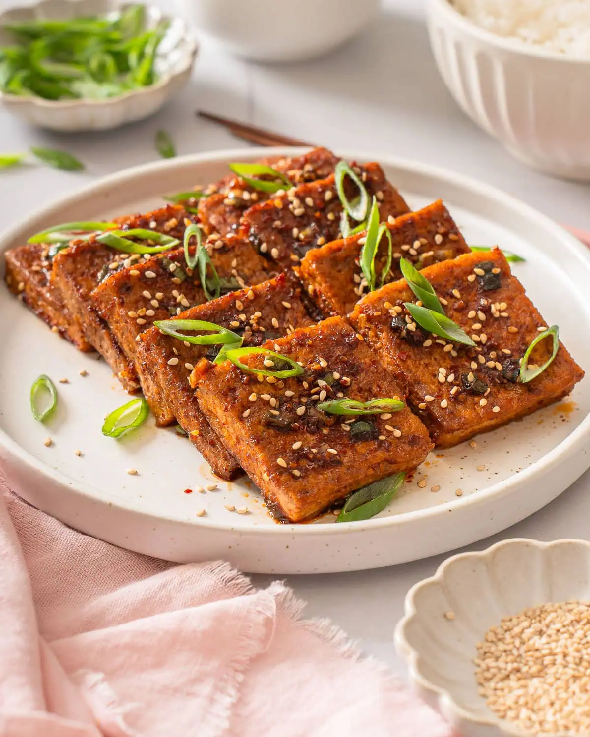 A plate of Korean braised tofu surrounded by table settings.